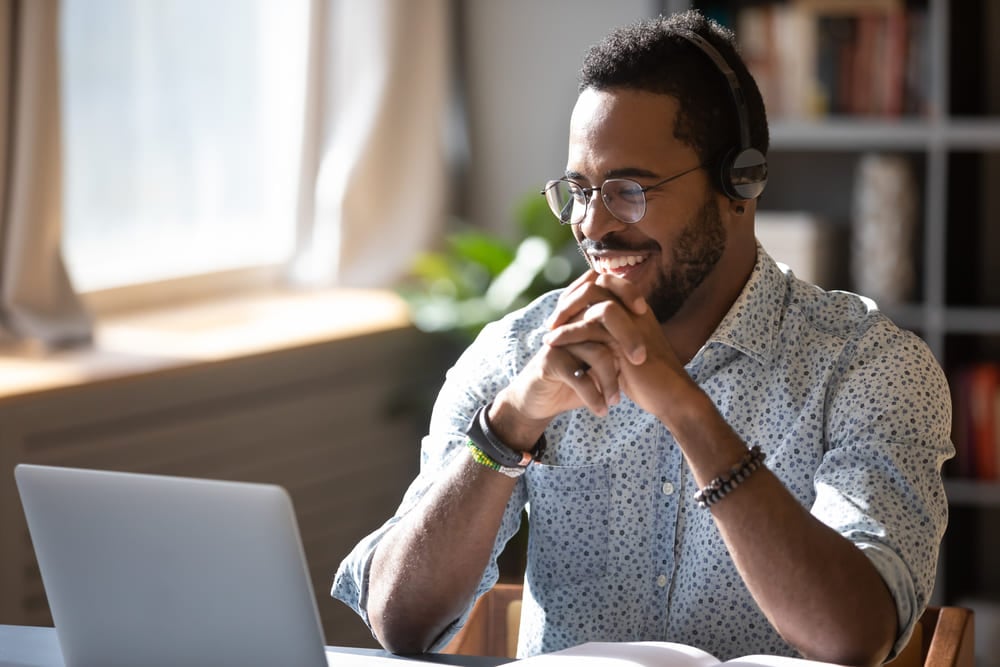 Na imagem vemos um rapaz afrodescendente olhando para o computador e sorrindo.